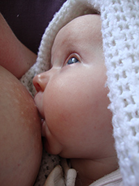 young baby getting breastfed is looking up at mum